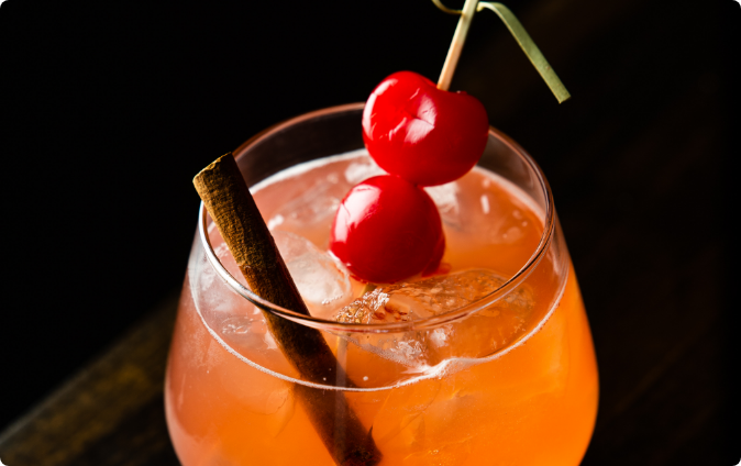 A mixed cocktail with cherries and a cinnamon stick